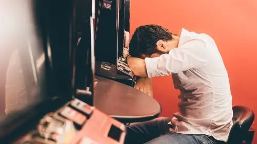 Glücksspielsucht – Symbolbild mit Person an Spielautomaten Person an einem Spielautomaten mit gesenktem Kopf – Symbolbild für Glücksspielsucht und deren Auswirkungen