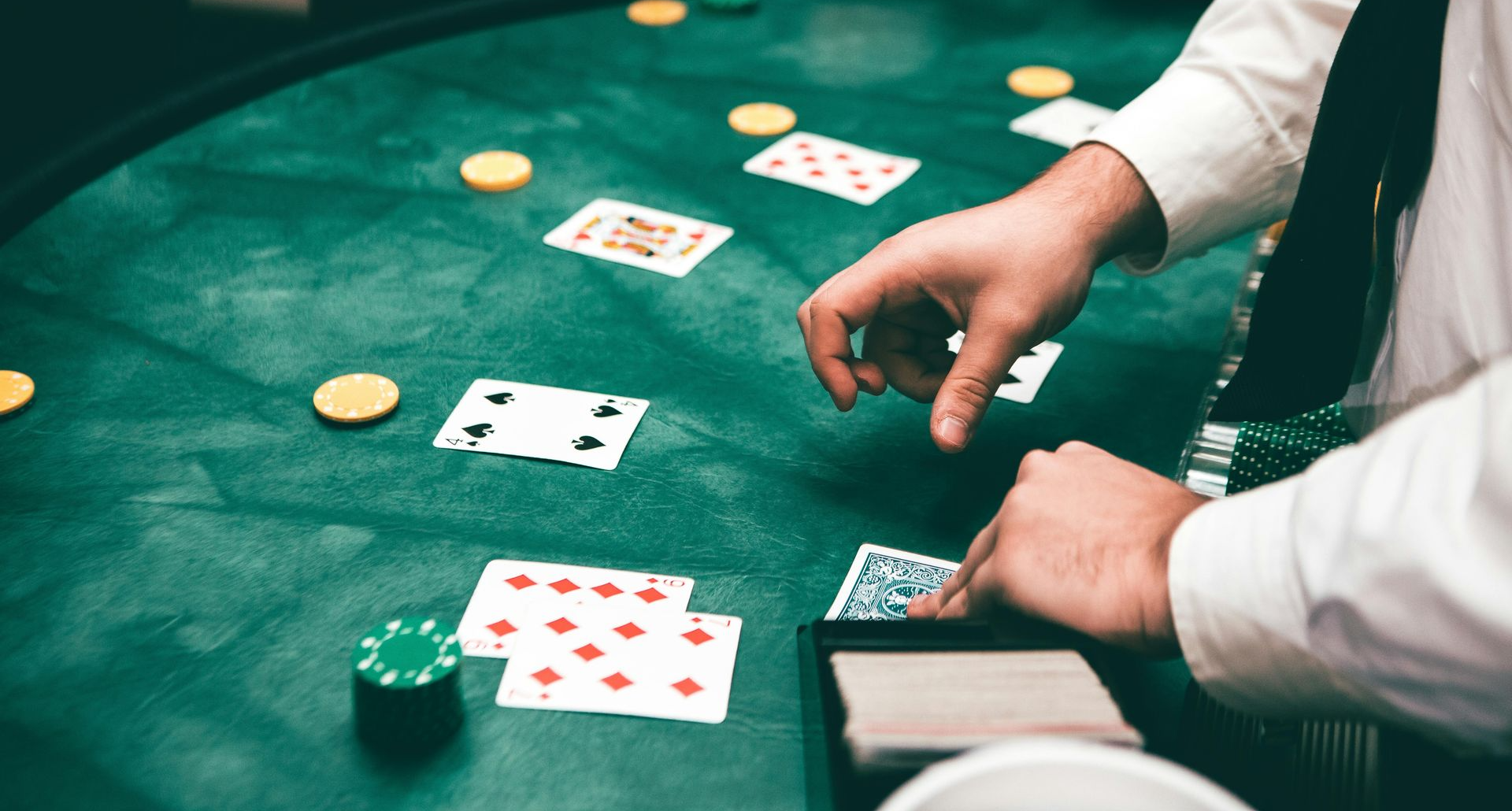Person mischt Karten an einem Casinotisch auf dem Spielkarten und Jetons liegen