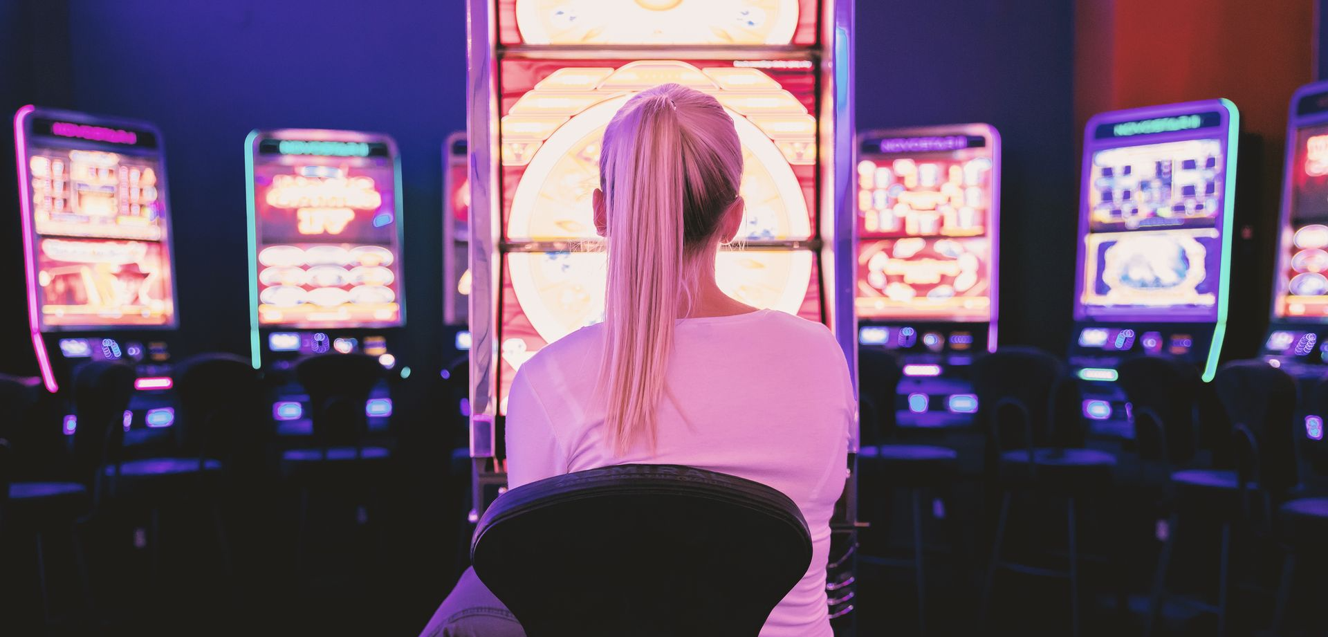 Person in Spielhalle vor beleuchteten Spielautomaten als Darstellung von Glücksspielumgebung